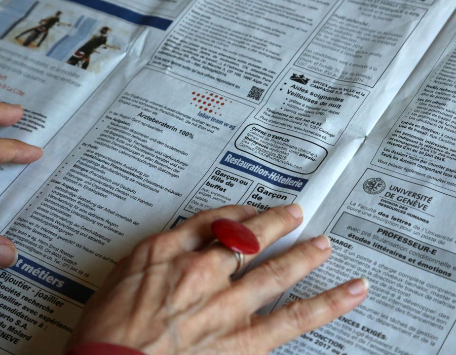 Les mains du femme âgée parcourent les petites annonces emploi d'un journal.