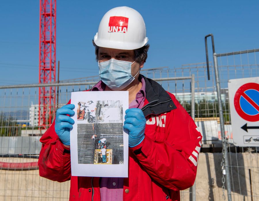 Secrétaire syndical d'Unia portant un masque présente une photographie montrant des travailleurs à l'oeuvre les uns à côté des autres.