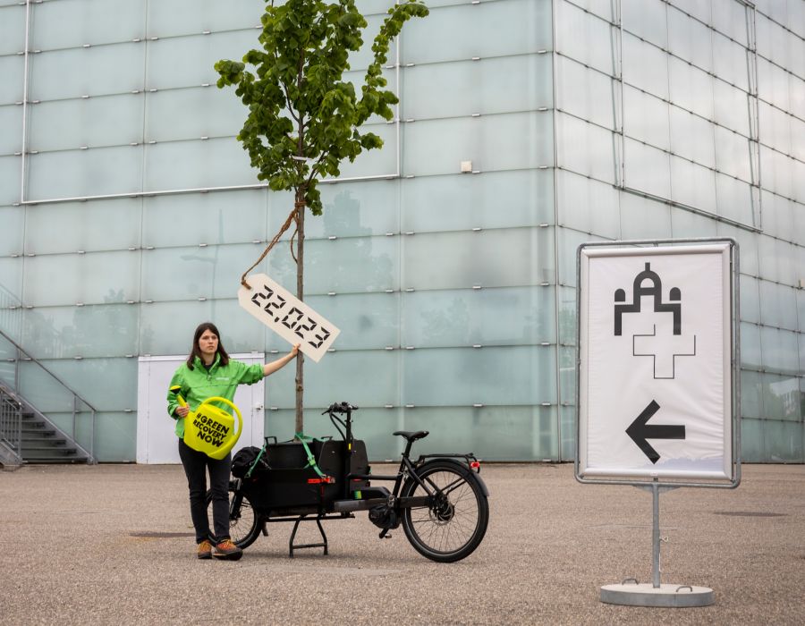 Une jeune femme devant BernExpo avec un arbre posé sur un vélo.