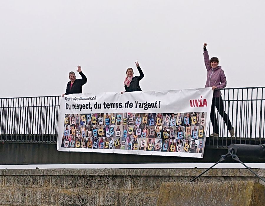 Sur un pont, trois femmes accrochent une banderole sur laquelle on peut lire: Du respect, du temps, de l'argent!