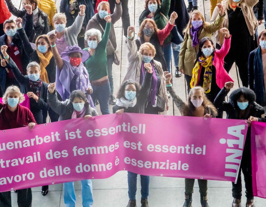Les déléguées des groupes d'intérêt femmes d'Unia, poing levé, derrière une banderole "Le travail des femmes est essentiel".