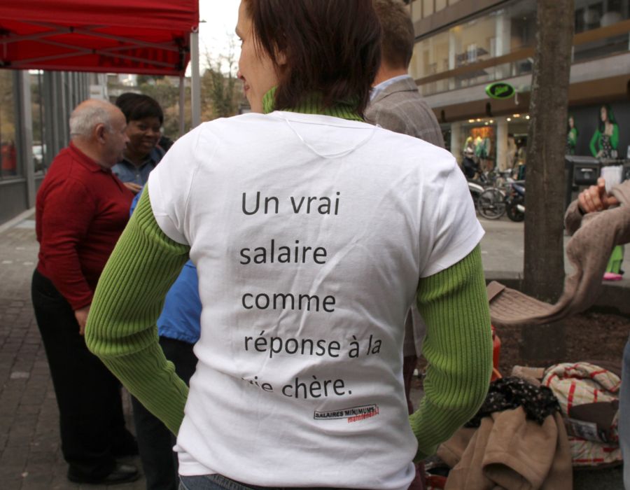 Une femme de dos. Sur son t-shirt blanc, il est écrit: "un vrai salaire comme réponse à la vie chère"