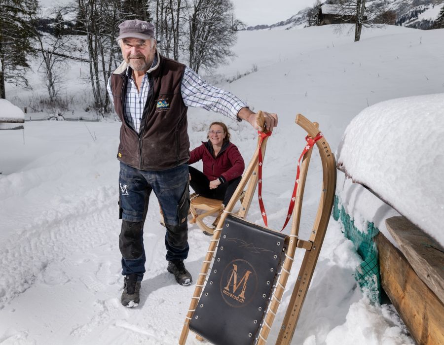 Bruno Morerod, dans la neige, présente une de ses luges. Derrière sa fille assise sur une autre.