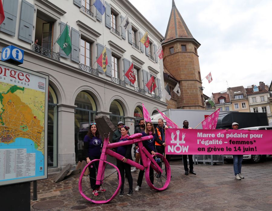 Une équipe d'Unia avec un gros vélo rose et une banderole sur laquelle on peut lire: Marre de pédaler pour l'égalité.