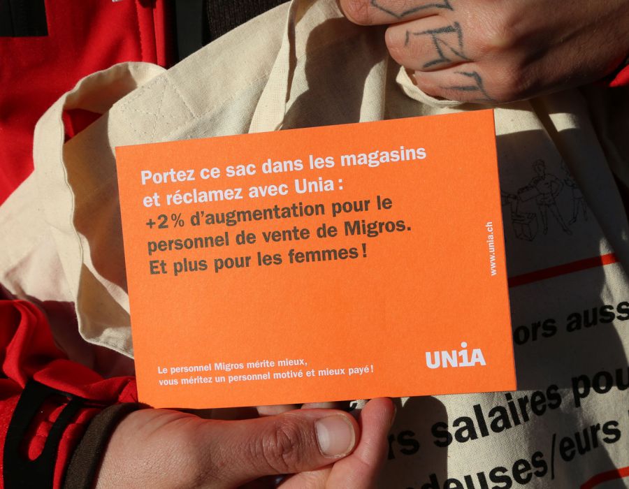 Flyer sur lequel on peut lire: Portez ce sac dans les magasins et réclamez avec Unia: +2% d'augmentation pour le personnel de vente de Migros. Et plus pour les femmes!
