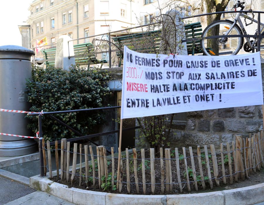 Devant des toilettes publiques, une banderole sur laquelle on peut lire: WC fermés pour cause de grève. 3000 francs par mois. Stop aux salaires de misère. Halte à la complicité entre la ville et Onet.