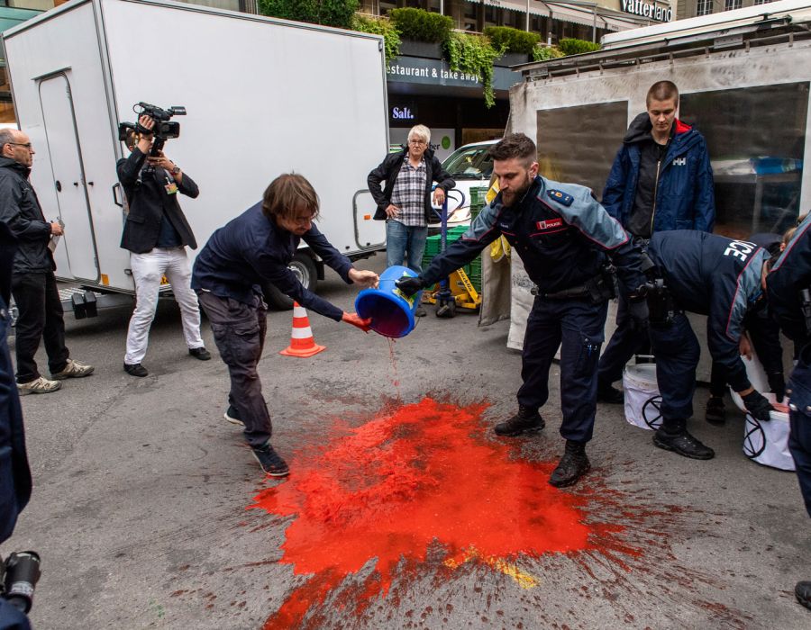 Manifestants déversant un liquide rouge dans la rue.