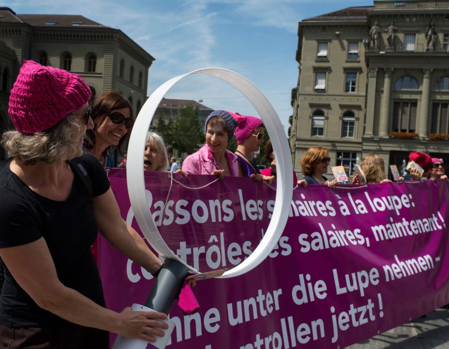 Manifestation féministe avec une pancarte sur laquelle on peut lire: "Passons les salaires à la loupe: contrôles des salaires maintenant!"