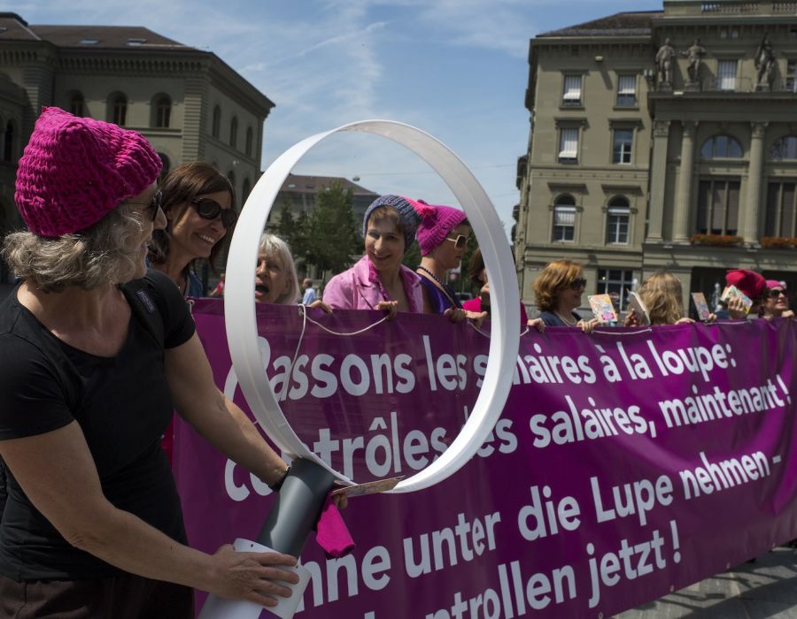 Action féministe à Berne avec une loupe géante et une banderole sur laquelle on peut lire: Passons les salaires à la loupe!
